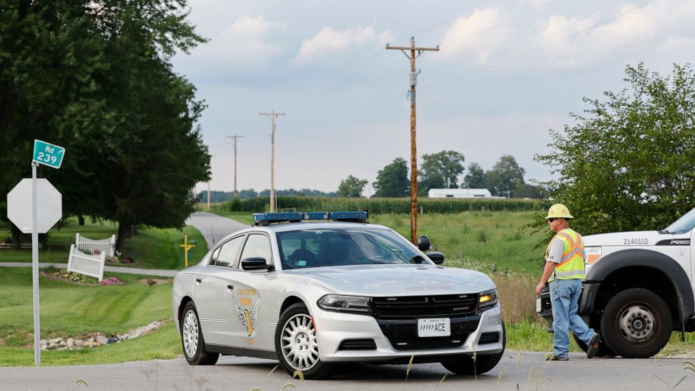 A Clinton County employee helps direct traffic as an Ohio State Highway Patrol vehicle leaves the scene where an armed man was shot and killed by police after breaching the FBI's Cincinnati field office Thursday, Aug. 11, 2022, in Wilmington, Ohio. (