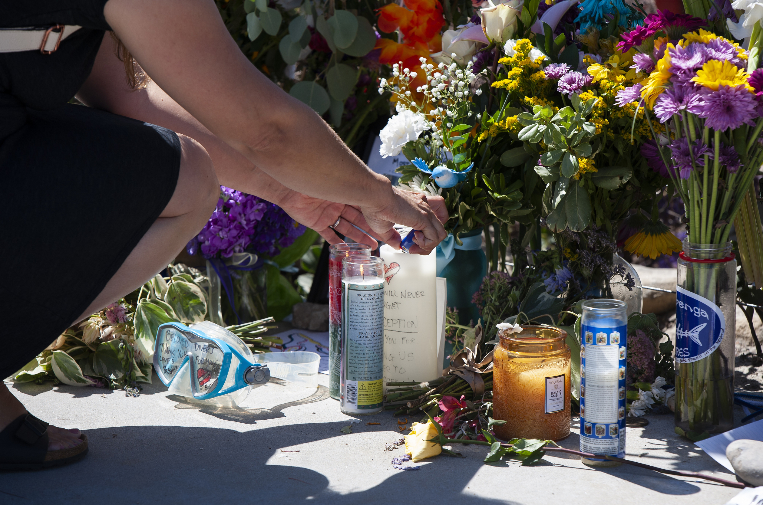 A woman relights a candle placed at a memorial for the victims of the Conception dive boat on the Santa Barbara Harbor on Sunday, Sept. 8, 2019 in Santa Barbara, Calif. Authorities served search warrants Sunday at the Southern California company that