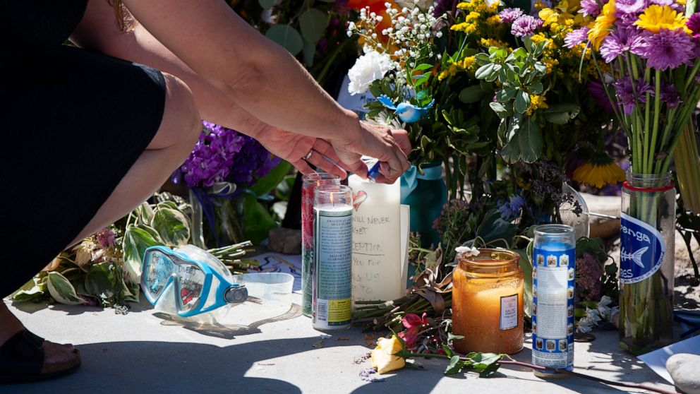 A woman relights a candle placed at a memorial for the victims of the Conception dive boat on the Santa Barbara Harbor on Sunday, Sept. 8, 2019 in Santa Barbara, Calif. Authorities served search warrants Sunday at the Southern California company that