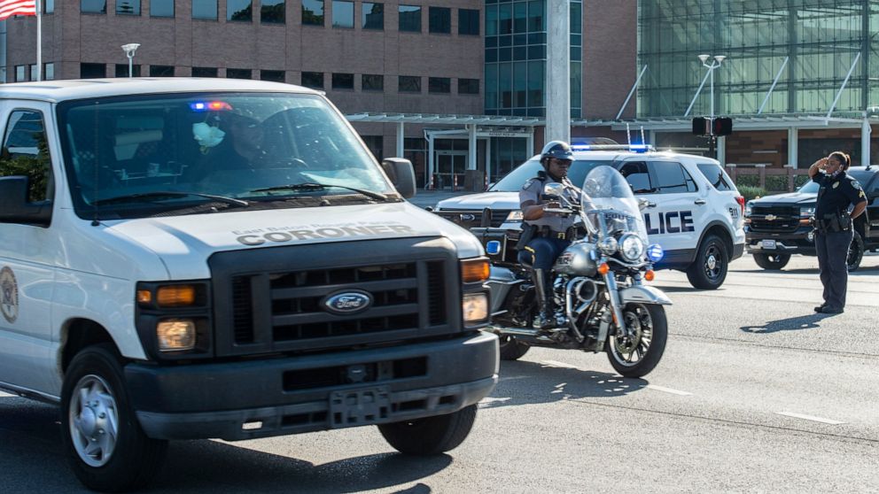 An officer salutes a motorcycle escort and a coroner's van carrying the body of a Baton Rouge police officer who was fatally shot, Sunday afternoon, April 26, 2020, in Baton Rouge, La. The shooting left one police officer dead and a wounded colleague