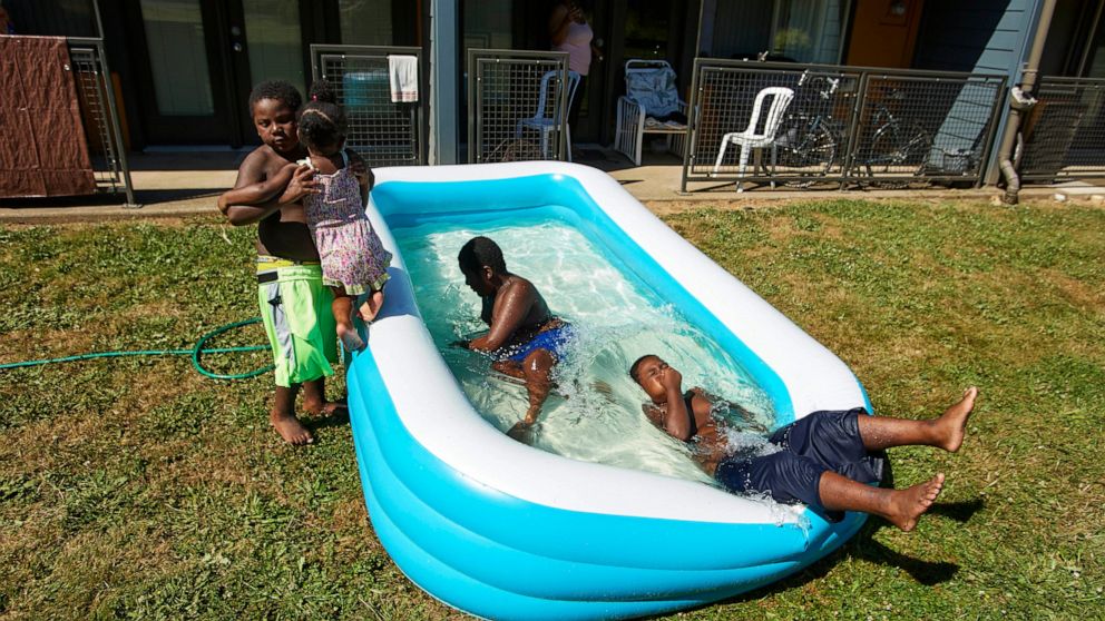Jalen Askari, 7, right, plugs his nose as he falls into the pool he is playing in with his siblings, from left, Amari, 5, Bella, 2, and DJ, 10, in Portland, Ore., Tuesday, July 26, 2022. Temperatures are expected to top 100 degrees F (37.8 C) on Tues