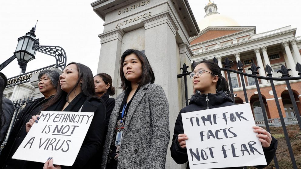 FILE- In this March 12, 2020 file photo, Jessica Wong, front left, Jenny Chiang, center, and Sheila Vo, from the state's Asian American Commission, stand together during a protest on the steps of the Statehouse in Boston. With a virtual event schedul