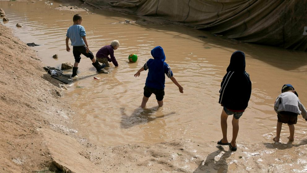 FILE - In this March 31, 2019 file photo, children play in a mud puddle in the section for foreign families at Al-Hol camp in Hasakeh province, Syria. The United Nations Children’s Fund on Monday, Dec. 7, 2020, launched a global appeal for a record $