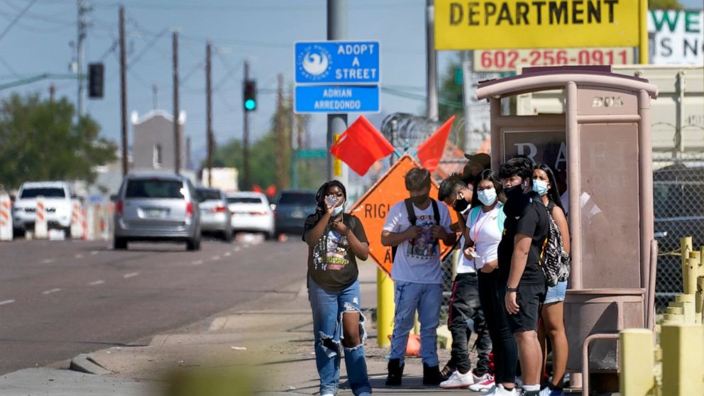 People stand in the direct sunlight adjacent to an over-crowded bus stop, Monday, Sept. 13, 2021, in Phoenix. Soaring temperatures are making it harder to live in the United States' already hot, fast growing desert areas. Heat dangers are even more p