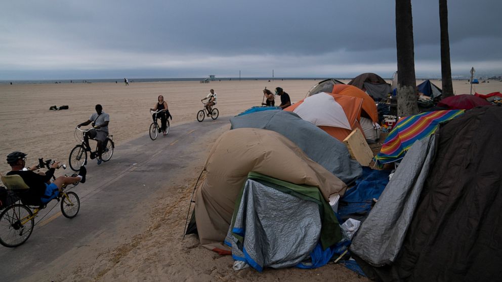 People ride their bikes past a homeless encampment set up along the boardwalk in the Venice neighborhood of Los Angeles, Tuesday, June 29, 2021. The proliferation of homeless encampments on Venice Beach has sparked an outcry from residents and create