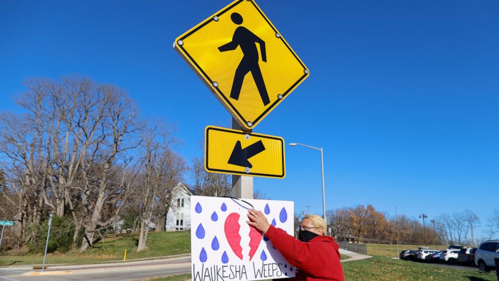 A woman puts up a sign outside City Hall in Waukesha, Wis., Monday, Nov. 22, 2021, after an SUV plowed into a Sunday Christmas parade, killing several and injuring dozens of others. (AP Photo/Jeffrey Phelps)