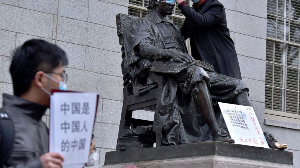 A man places a mask over the eyes of the John Harvard Statue in Harvard Yard as close to 100 students and faculty demonstrated against strict anti-virus measures in China, Tuesday, Nov. 29, 2022, at Harvard University in Cambridge, Mass. Protests in 
