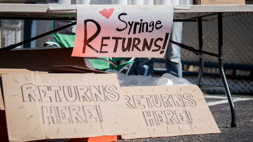 In this photo provided by Chad Cordell, signs for syringe returns are shown Saturday, March 6, 2021, at a nonprofit group's health fair in Charleston, W.Va. For years, West Virginia has had the nation's highest rate of drug overdose deaths. Now the s