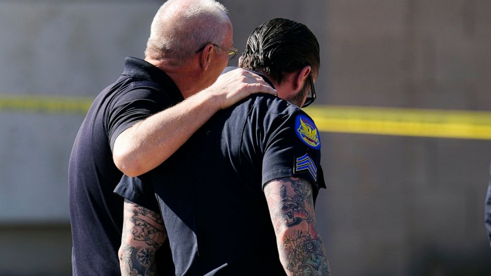 Police officers comfort one another in front of a house where several Phoenix Police Department officers were shot and four others were injured after responding to a shooting inside the home Friday, Feb. 11, 2022, in Phoenix. The shooting suspect was