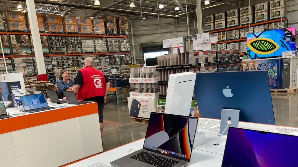 A sales associate helps a prospective customer as laptops sit on display in a Costco warehouse, Aug. 15, 2022, in Sheridn, Colo. Americans picked up their spending a bit in August from July even as surging inflation on household necessities like rent