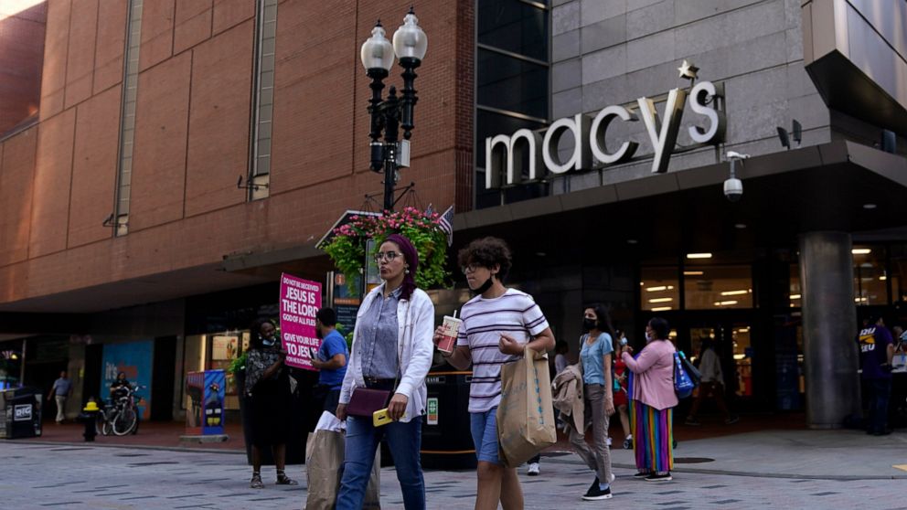 FILE - In this July 14, 2021 file photo, pedestrians pass the Macy's store in the Downtown Crossing shopping area, in Boston. Americans cut back on their spending last month as a surge in COVID-19 cases kept people away from stores. Retail sales fell