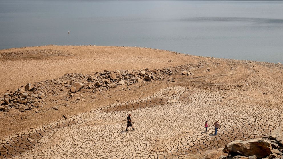 FILE — In this Aug. 22, 2021, file photo, a family walks over cracked mud near Lake Oroville's shore as water levels remain low due to continuing drought conditions in Oroville, Calif. State water officials are preparing to tell major urban and agric