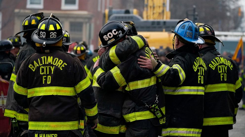 FILE - Firefighters embrace each other after a deceased firefighter was pulled out of a building collapse while battling a two-alarm fire in a vacant row home, Monday, Jan. 24, 2022, in Baltimore. Officials said several firefighters died during the b