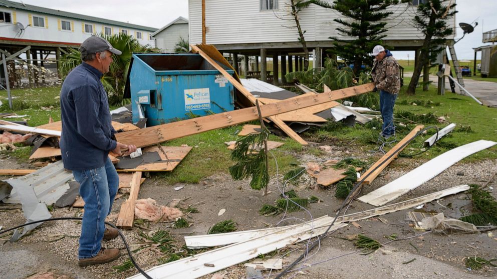 FILE - In this Friday, Oct. 30, 2020, file photo, Mark Andollina, left, and Shane Holder, remove part of a roof damaged by Hurricane Zeta from the road at the Cajun Tide Beach Resort in Grand Isle, La. The late-hitting Hurricane Zeta has been upgrade