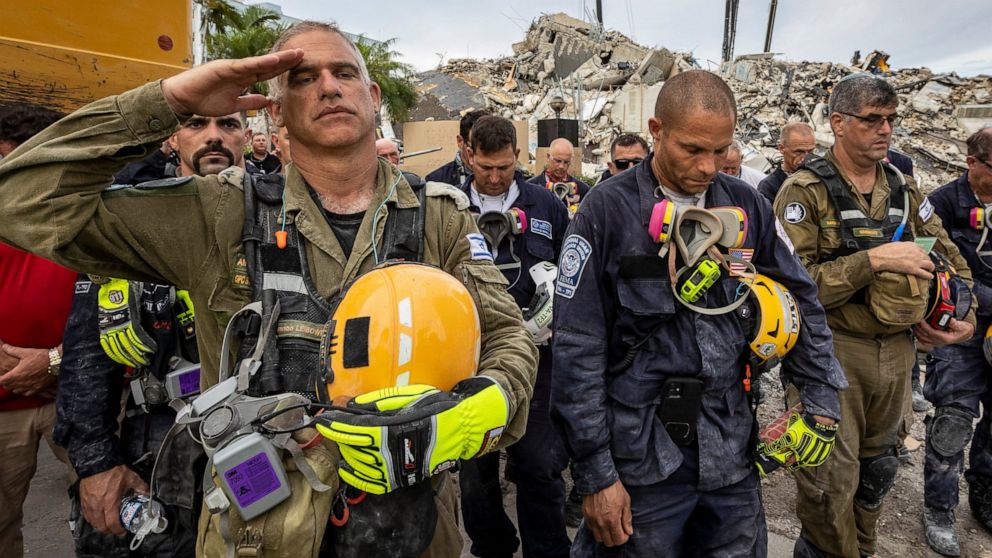 FILE - A member of the Israeli search and rescue team, left, salutes in front of the rubble that once was Champlain Towers South during a prayer ceremony, Wednesday, July 7, 2021, in Surfside, Fla. The Israeli search and rescue team that arrived in S