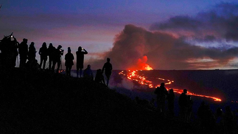 FILE - People watch and record images of lava from the Mauna Loa volcano Thursday, Dec. 1, 2022, near Hilo, Hawaii. Officials monitoring the Mauna Loa eruption on Hawaii's Big island said Wednesday, Dec. 7, the lava flow moving toward state Route 200