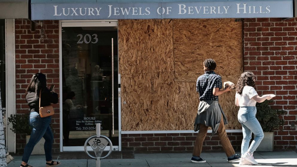 Pedestrians walk past a boarded up Luxury Jewels of Beverly Hills on Wednesday, March 23, 2022 in Beverly Hills, Calif. Los Angeles police are warning people that wearing expensive jewelry in public could make them a target for thieves — a note of ca