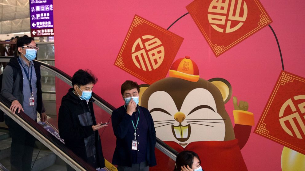 People wear face masks as they ride an escalator at the Hong Kong International Airport in Hong Kong, Tuesday, Jan. 21, 2020. Face masks sold out and temperature checks at airports and train stations became the new norm as China strove Tuesday to con