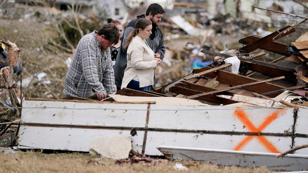 FILE -Brandon Clark, behind, injured from the tornado, returns to his destroyed home for the first time with Laura Shepherd, Tyler Shepherd, left, and his wife Georgialee Clark, behind in the aftermath of tornadoes that tore through the region, in Da
