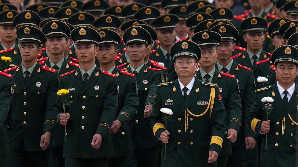 Paramilitary policemen and military officers hold flowers walk to pay respects to the People's Heroes Monument during a ceremony to mark Martyr's Day at Tiananmen Square in Beijing, Thursday, Sept. 30, 2021. Chinese President Xi Jinping paid respects