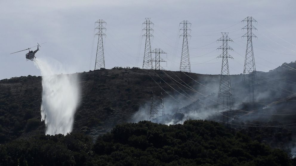 FILE - In this Oct. 10, 2019, file photo, a helicopter drops water near power lines and electrical towers while working at a fire on San Bruno Mountain near Brisbane, Calif. California energy leaders on Friday, May 6, 2022 said the state may see an e