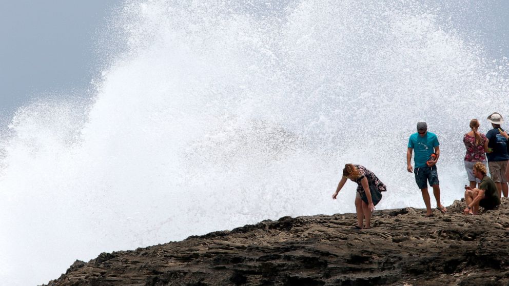 FILE — In this July 26 2020 file photo, people react as a wave breaks off rocks in Laie, Hawaii, as Hurricane Douglas passed by the state. The central Pacific basin, including Hawaii, can expect between two and five tropical depressions, tropical sto