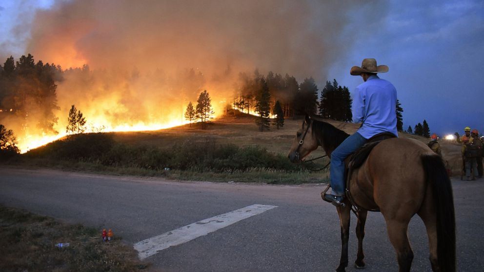 FILE - Rowdy Alexander watches from atop his horse as a hillside burns on the Northern Cheyenne Indian Reservation on Aug 11, 2021, near Lame Deer, Mont. An area outside Denver where Colorado's most destructive in history wildfire burned 1,000 homes 
