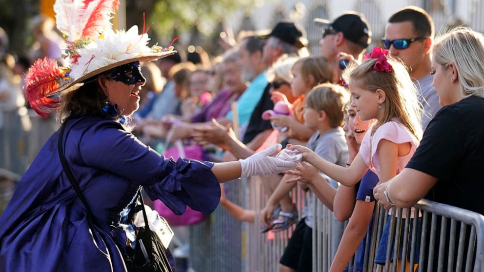 FILE - A woman dressed in period costume hands a trinket to a child during a parade dubbed "Tardy Gras," to compensate for a cancelled Mardi Gras due to the COVID-19 pandemic, in Mobile, Ala., on May 21, 2021. Mobile, Alabama’s first big parade of th