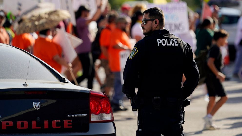 FILE - A Uvalde police officer watches as family and friends of those killed and injured in the school shootings at Robb Elementary take part in a protest march and rally, Sunday, July 10, 2022, in Uvalde, Texas. Four months after the Robb Elementary