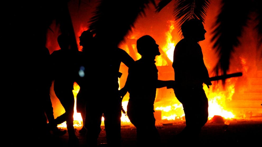 FILE - In this Friday, Sept. 21, 2012, file photo, civilians watch fires at an Ansar al-Shariah Brigades compound after hundreds of locals, military, and police raided the Brigades base in Benghazi, Libya. The warring parties in Libya and their inter