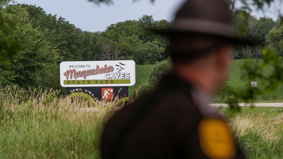 An Iowa State Patrolman walks past a Maquoketa Caves State Park sign as police investigate a shooting that left several people dead, Friday, July 22, 2022, in Maquoketa, Iowa. The campground was evacuated in the wake of the shooting. (Nikos Frazier/Q