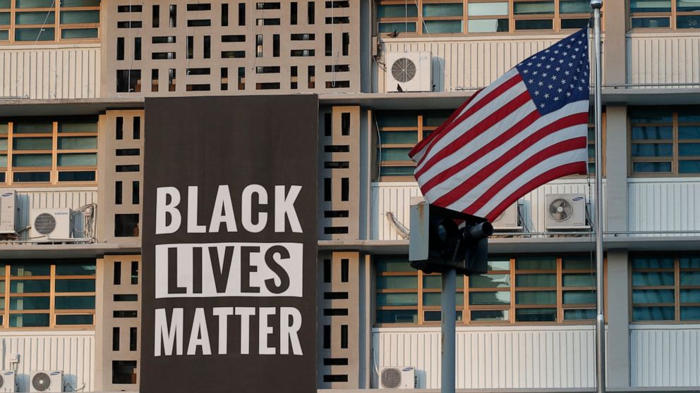 In this June 14, 2020 photo, U.S. flag flutters next to a giant Black Lives Matter banner at the U.S. Embassy in Seoul, South Korea. The banner has been removed from the U.S. Embassy building in South Korea's capital three days after it was raised th