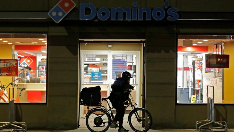 FILE - A delivery worker leaves a Domino's Pizza restaurant in downtown Seattle on a bike, Sunday, March 15, 2020. Domino’s Pizza says shortages of cooks, drivers and other staff are pinching sales at its U.S. stores. The world’s largest pizza chain 