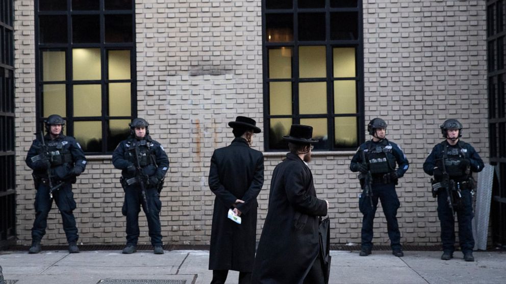 FILE - In this Dec. 11, 2019 file photo, Orthodox Jewish men pass New York City police guarding a Brooklyn synagogue prior to a funeral for Mosche Deutsch in New York. Deutsch, a rabbinical student from Brooklyn, was killed in the shooting inside a J
