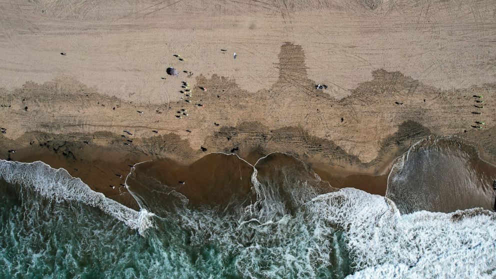 FILE - This aerial photo taken with a drone, shows beachgoers as workers in protective suits continue to clean the contaminated beach in Huntington Beach, Calif., on Oct. 11, 2021. Officials were investigating an oil sheen spotted Saturday, Nov. 20, 