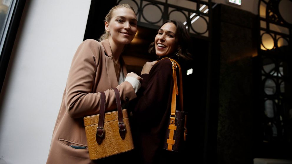 FILE - In this Feb. 24, 2019 file photo, model Arizona Muse, left, is flanked by designer and Officina del Poggio owner Allison Hoeltzel Savini as they present a creation of the Officina del Poggio women's Fall-Winter 2019-2020 collection, in Milan, 