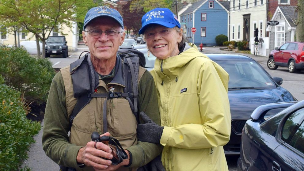 In this Wednesday, May 15, 2019 photo, U.S. Air Force veteran William Shuttlesworth, left, poses with his wife Patty on Market Street, in Newburyport, Mass., at the start of his planned cross-country hike to raise awareness for veterans' issues. Shut