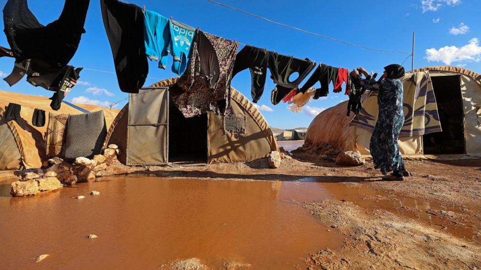 FILE - A woman hangs laundry in a flooded refugee camp in Idlib province, Syria, Dec. 21, 2021. Syrians in the last major rebel stronghold in the war-ton country are living in fear of the effects of Russia closing down the only border crossing into t