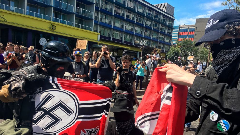 FILE - In this Aug. 4, 2018, file photo, counter protesters tear a Nazi flag, in Portland, Ore. A member of Portland's city council says she is shocked by a newspaper report that the commander for the police rapid response team exchanged friendly tex