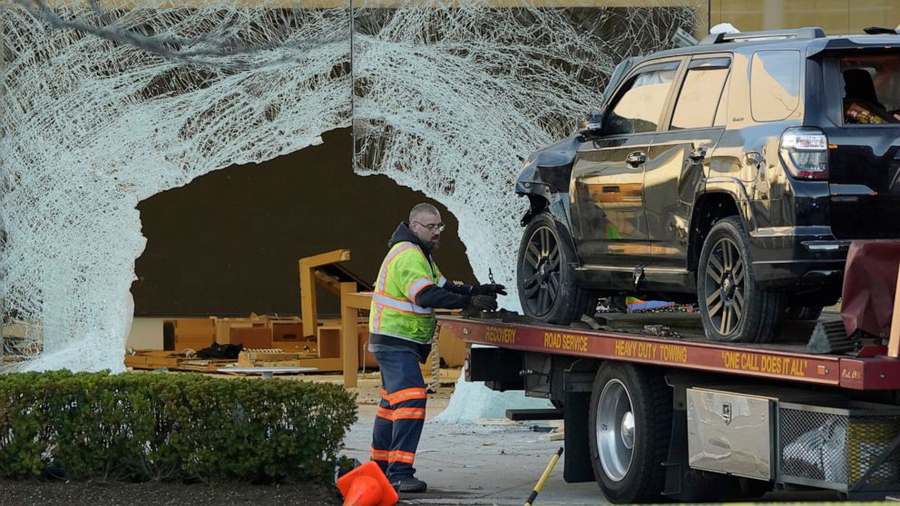 A worker secures a damaged SUV to a flatbed tow truck outside an Apple store, Monday, Nov. 21, 2022, in Hingham, Mass. At least one person was killed and multiple others were injured Monday when the SUV crashed into the store, authorities said. The c