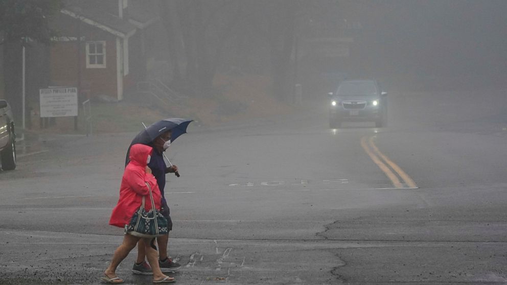 Two people cross the road as wind and rain pummel the area Friday, Sept. 9, 2022, in Julian, Calif. A tropical storm nearing Southern California has brought fierce mountain winds, high humidity, rain and the threat of flooding to a region already dea