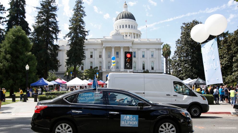 FILE - In this Aug. 28, 2019, file photo dozens of supporters of a measure to limit when companies can label workers as independent contractors circle the Capitol during a rally in Sacramento, Calif. California is suing ride-hailing companies Uber an
