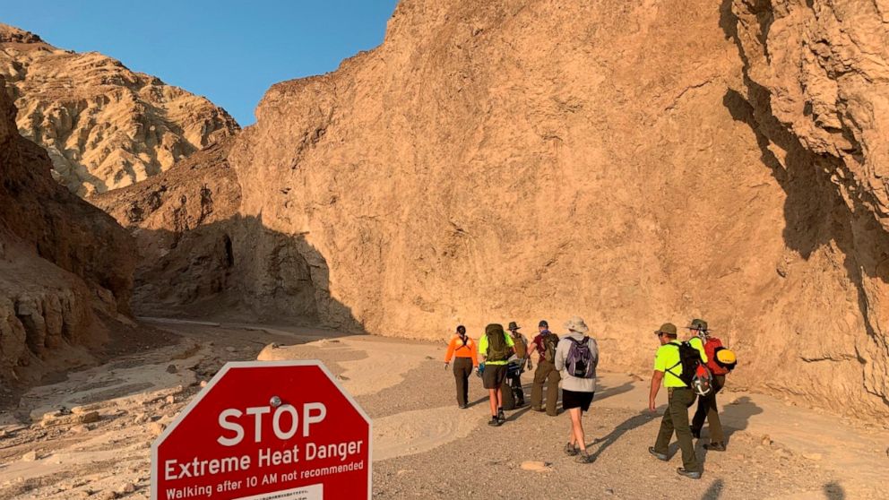 In this Wednesday, Aug. 18, 2021, photo provided by the National Park Service, an inter-agency search and rescue crew walks past a sign reading" "Stop, Extreme Heat Danger," with park rangers responding on foot near Red Cathedral along the Golden Can