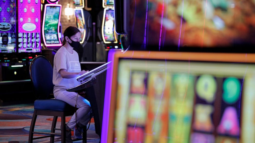 FILE - In this June 4, 2020, file photo, a woman plays an electronic slot machine at at the reopening of the Bellagio hotel and casino in Las Vegas. The coronavirus and efforts to fight it have hit U.S. casinos and legal gambling businesses hard. The