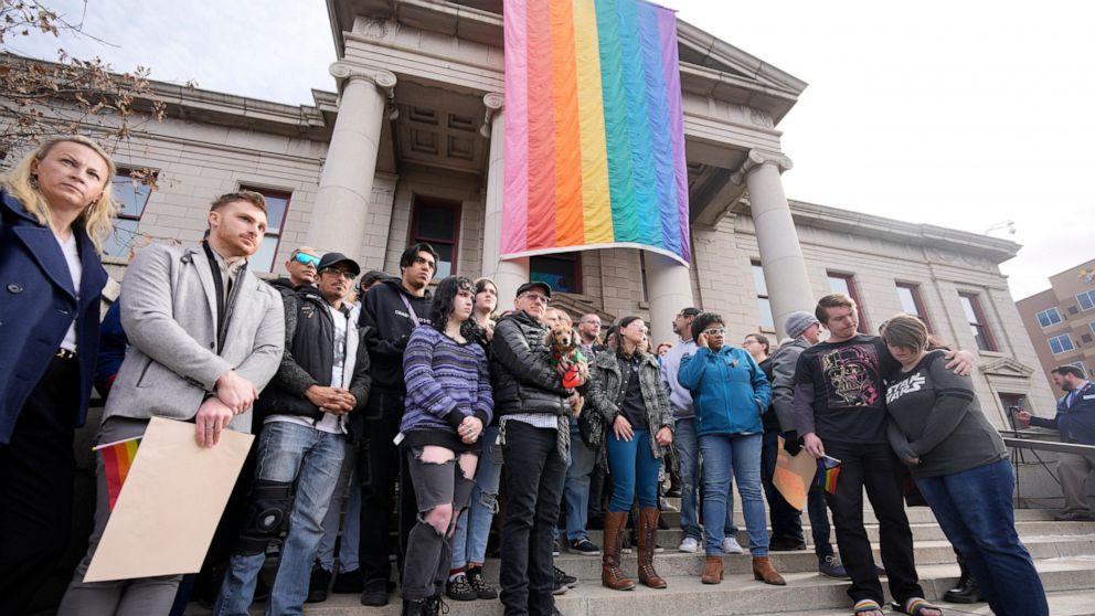 Supporters of Club Q stand beneath a 25-foot historic pride flag displayed on the exterior of city hall to mark the weekend mass shooting at a gay nightclub Wednesday, Nov. 23, 2022, in Colorado Springs, Colo. (AP Photo/David Zalubowski)