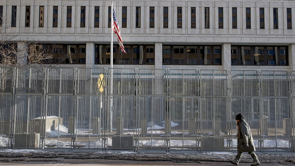 A pedestrian makes his way in front of a gated Warren E. Burger Federal Building as jury selection begins in St. Paul, Minn., Thursday, Jan. 20, 2021. Jury selection began Thursday in the federal trial of three Minneapolis police officers charged in 