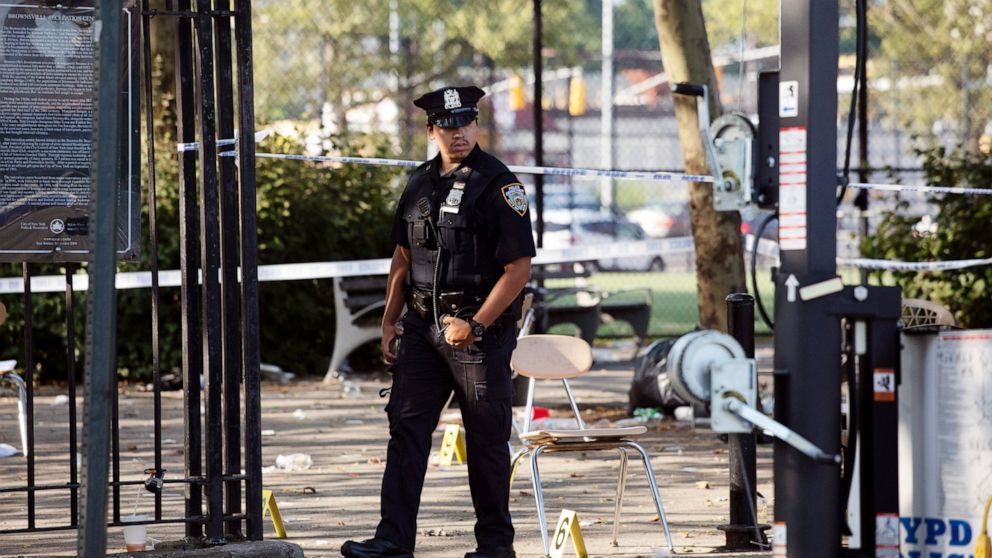 FILE - In this July 28, 2019 file photo, a police officer walks by yellow evidence markers at a playground after a shooting in the Brownsville neighborhood in the Brooklyn borough of New York. New York City police have made an arrest in the community