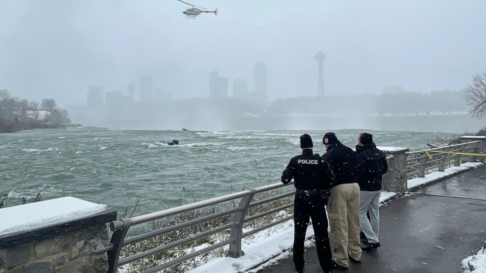 Authorities monitor a car partially submerged in the Niagara River near the brink of American Falls, Wednesday, Dec. 8, 2021, in Niagara Falls, N.Y. A U.S. Coast Guard diver was lowered from a hovering helicopter and pulled a body from the submerged 
