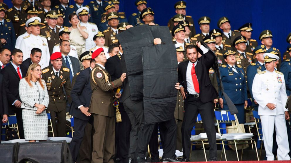 FILE - In this Aug. 4, 2018 file photo released by China's Xinhua News Agency, security guards surround Venezuelan President Nicolas Maduro with protective gear as an unidentified drone interrupts his speech in Caracas, Venezuela. An exiled Venezuela