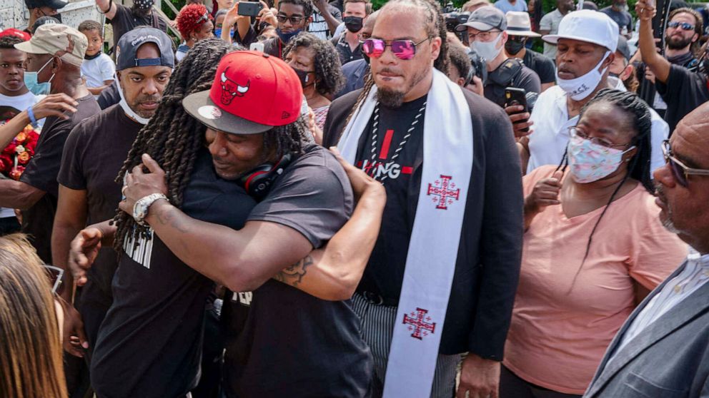 Local artist and business owner Ulysses Edwards, foreground wearing red Chicago Bulls cap, receives a hug from Khalil Ferebee, one of Andrew Brown Jr.'s sons, Sunday, May 2, 2021, in Elizabeth City, N.C., during a presentation of a mural honoring Bro